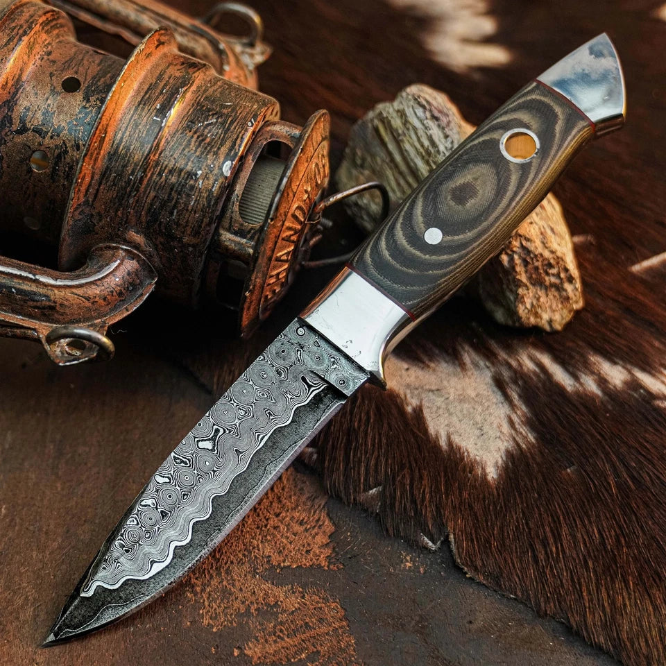A fixed-blade knife with a patterned steel blade and a dark wood handle with silver accents, displayed diagonally on a rustic brown surface with a metal container and wood pieces in the background.