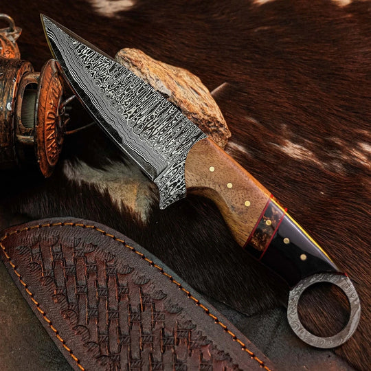 A fixed-blade knife with a patterned steel blade, a brown wood handle, and a black ring pommel, displayed diagonally on a brown and white cowhide surface next to a leather sheath.