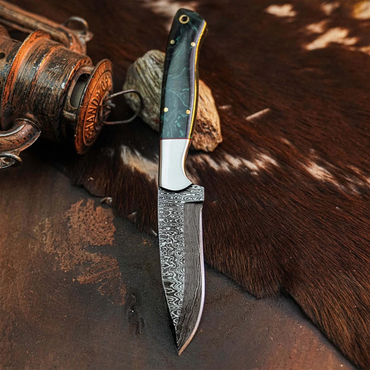 A custom fixed-blade knife with a Damascus steel blade and a dark green marbled handle, displayed on a rustic brown cowhide background next to a wooden spool.