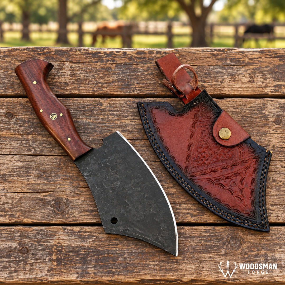 A handmade axe with a dark textured steel blade and a contoured wooden handle lies next to its custom carved reddish-brown leather sheath on a rustic wooden plank surface. The background shows a blurred outdoor scene with trees and a horse.