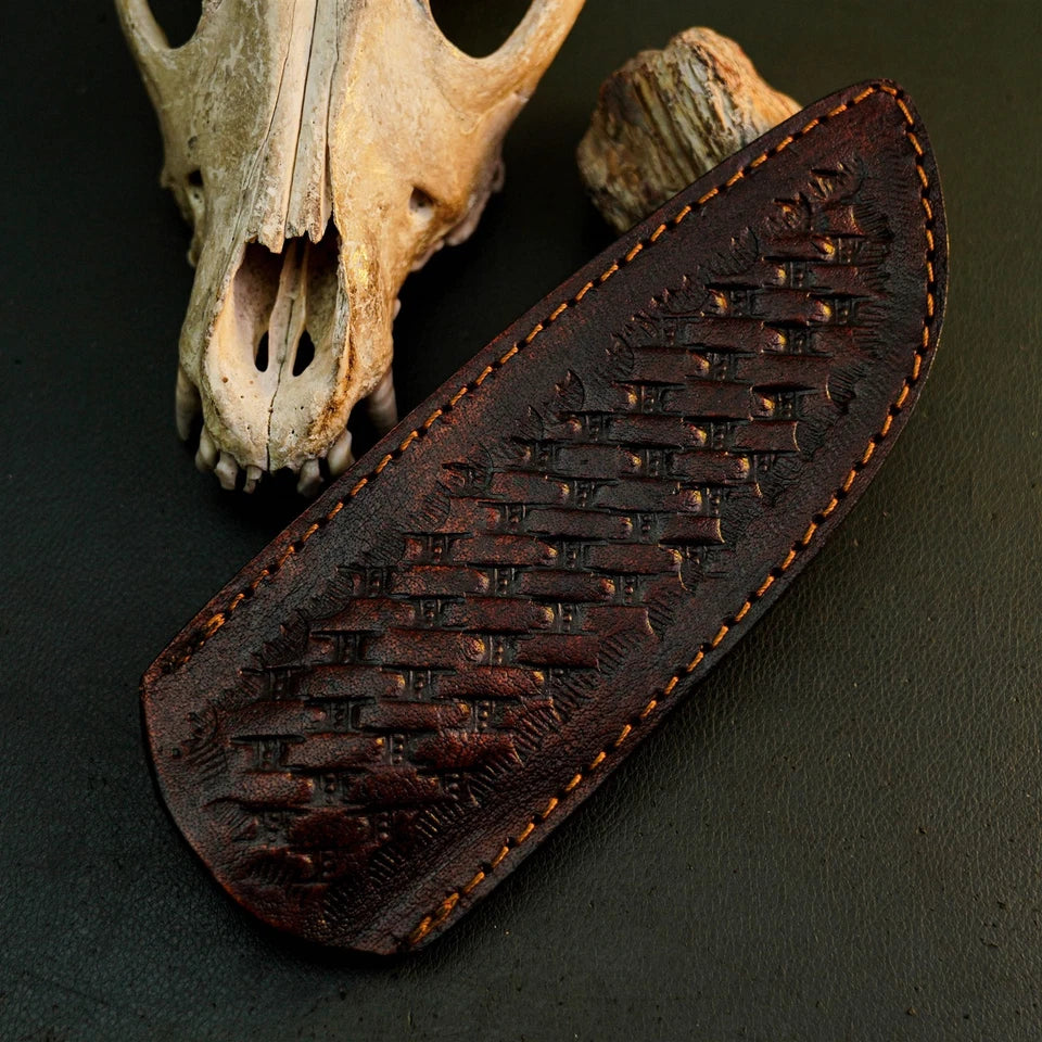 A dark brown leather sheath with an embossed basketweave pattern and contrast stitching, displayed on a dark textured surface next to animal skull and bone props.
