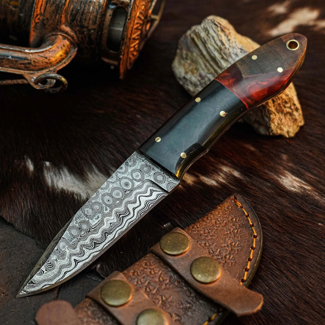 A fixed-blade knife with a patterned Damascus steel blade and a dark wood handle with brass pins, displayed on a brown fur surface next to a leather sheath and rustic props.