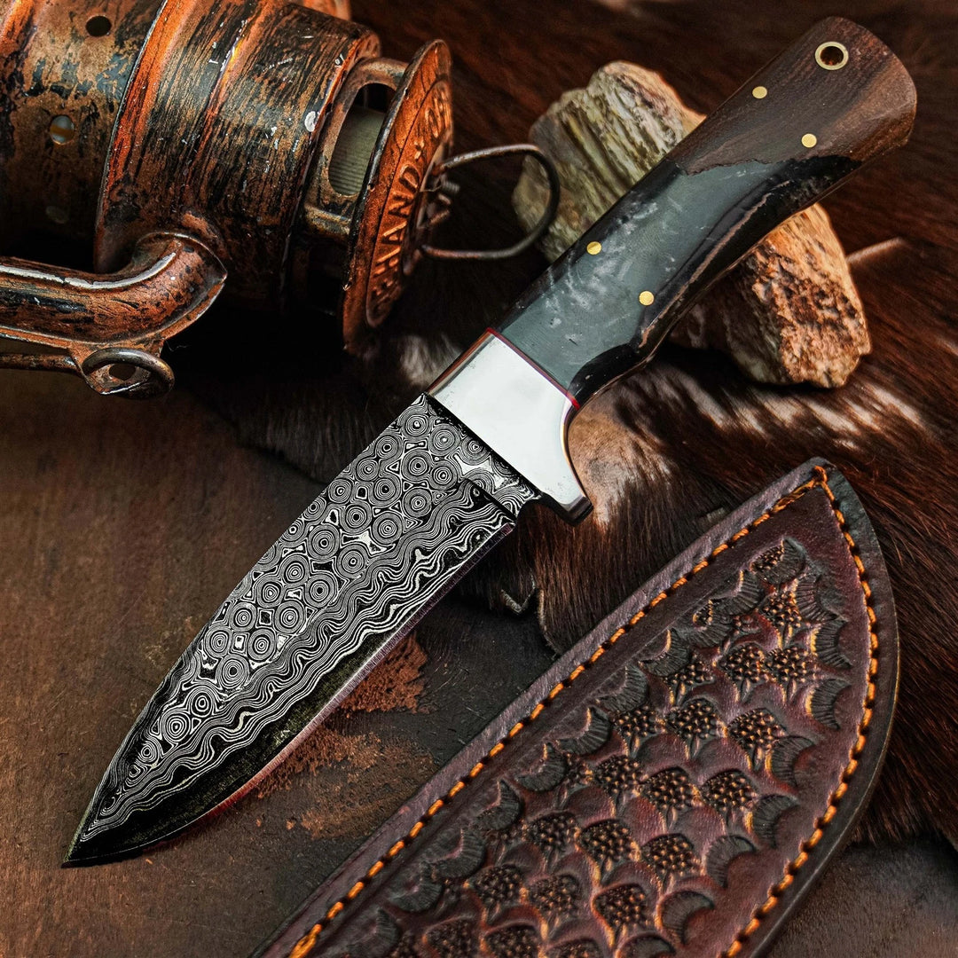 A Damascus steel fixed-blade knife with a patterned blade, dark handle, and brass pins, displayed diagonally next to its brown leather sheath on a rustic background with wood and fur.