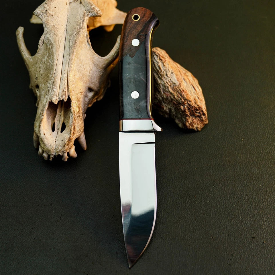 A fixed-blade knife with a polished steel blade and a dark wood handle with metal rivets, displayed upright on a dark textured surface next to animal bones.