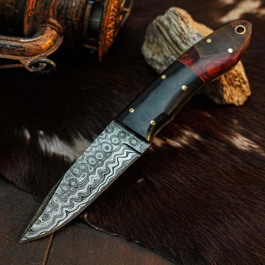 A fixed-blade knife with a patterned Damascus steel blade and a dark handle, displayed diagonally on a dark brown fur surface with rustic props.