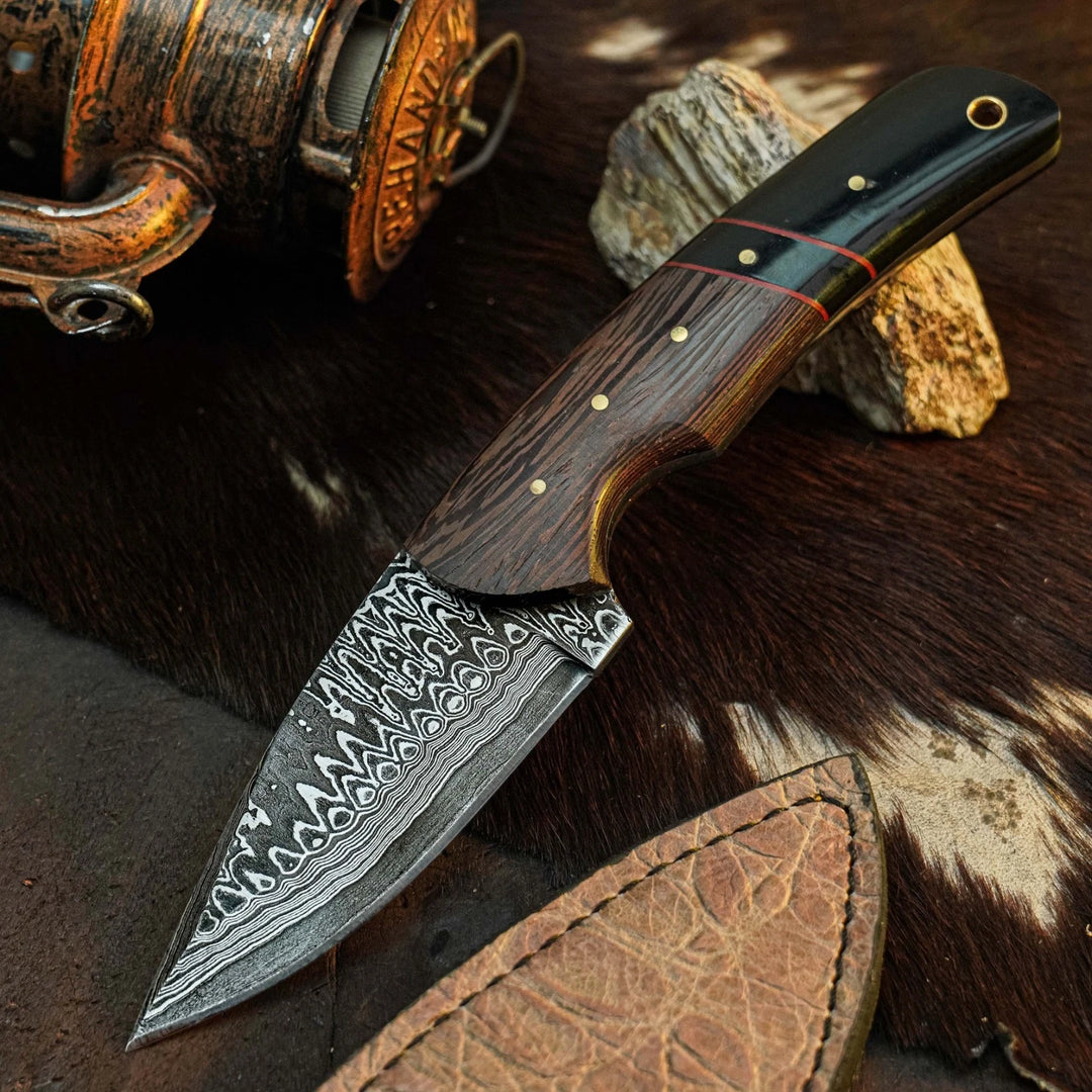 A fixed-blade knife with a patterned Damascus steel blade, a dark wood handle, and a black pommel, displayed diagonally on a brown fur surface with a leather sheath and rustic props.