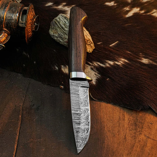 A fixed-blade knife with a patterned Damascus steel blade and a dark wood handle, resting on a brown and white cowhide rug over a wooden surface.